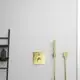 Wandmontiertes Duschthermostat in Goldoptik von Ideal Standard, mit Bedienknopf und Handbrause. Neben einem schwarzen Regal für Pflegeprodukte an der Wand.